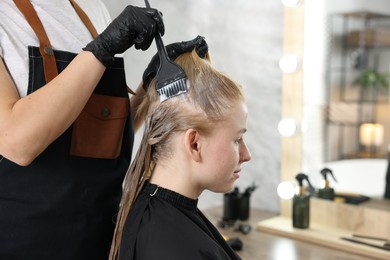 Photo of Hairdresser applying dye on woman's hair in salon, closeup