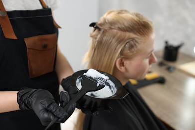 Photo of Hairdresser applying dye on woman's hair in salon, closeup