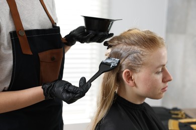 Photo of Hairdresser applying dye on woman's hair in salon, closeup