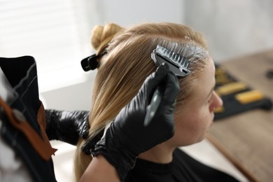 Photo of Hairdresser applying dye on woman's hair in salon, closeup