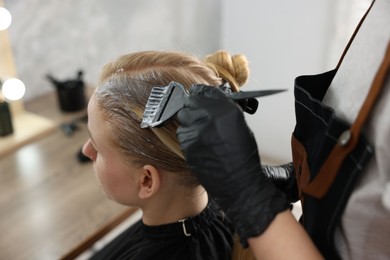 Photo of Hairdresser applying dye on woman's hair in salon, closeup