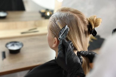 Photo of Hairdresser applying dye on woman's hair in salon, closeup
