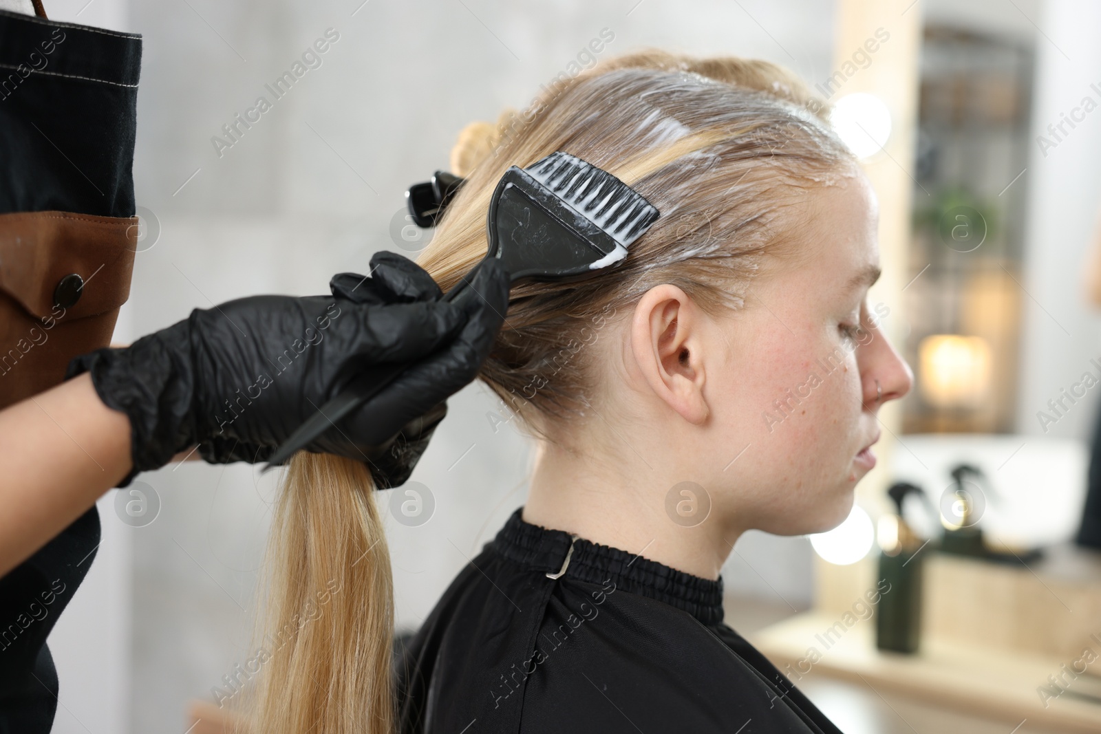 Photo of Hairdresser applying dye on woman's hair in salon, closeup