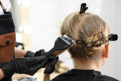 Photo of Hairdresser applying dye on woman's hair in salon, closeup