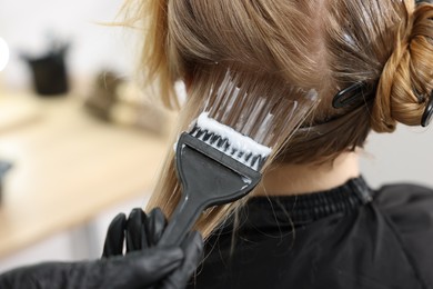Photo of Hairdresser applying dye on woman's hair in salon, closeup