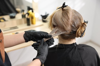 Photo of Hairdresser applying dye on woman's hair in salon, closeup