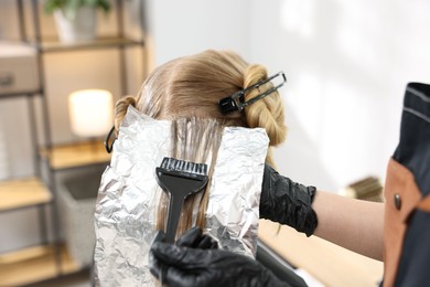 Photo of Hairdresser applying dye on woman's hair in salon, closeup
