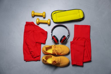Photo of Sportswear, sneakers, ankle weights, dumbbells and headphones on gray textured background, flat lay