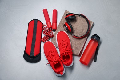 Photo of Sneakers, skipping rope, headphones and other accessories on gray textured background, flat lay