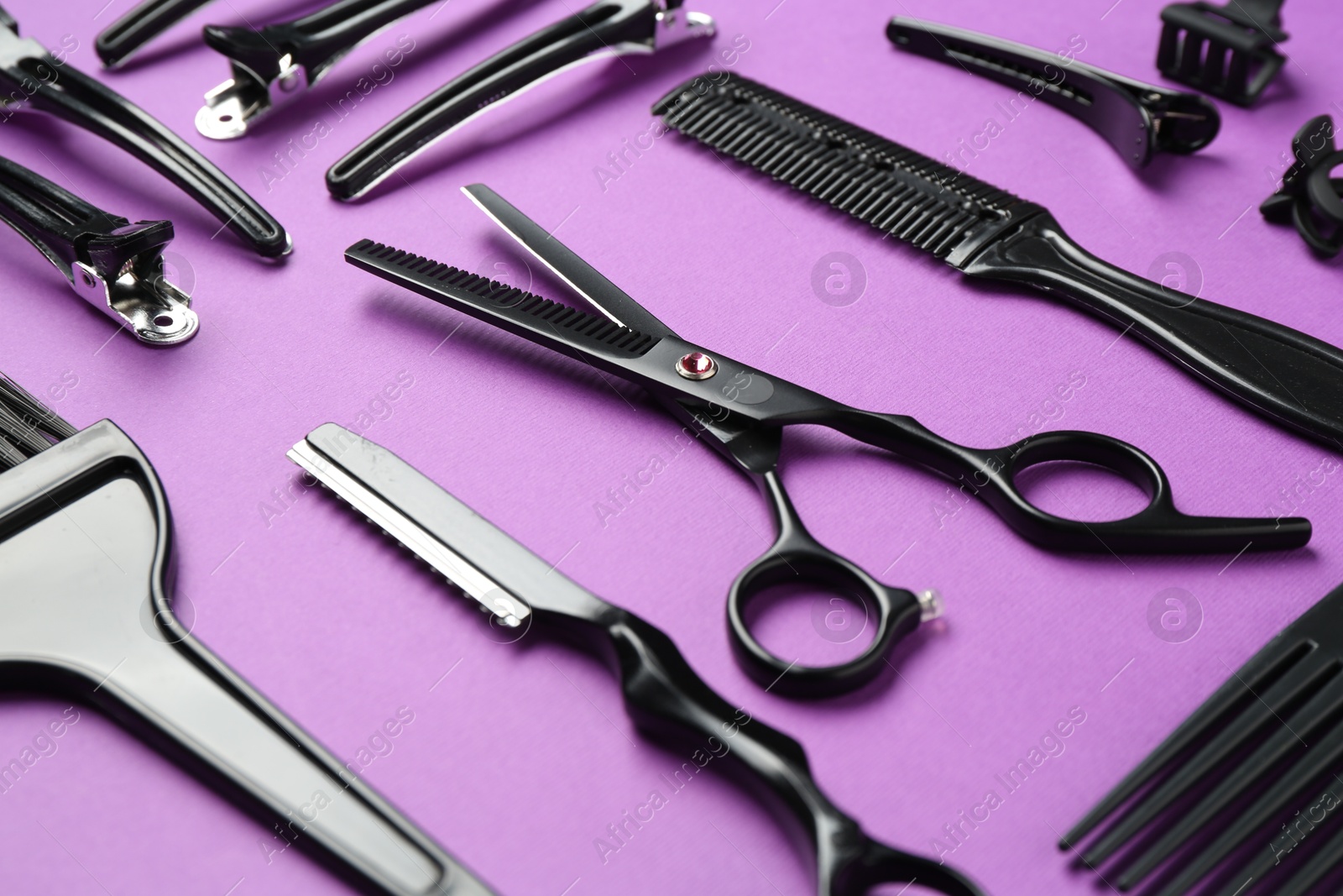 Photo of Different hairdresser's tools on violet background, closeup