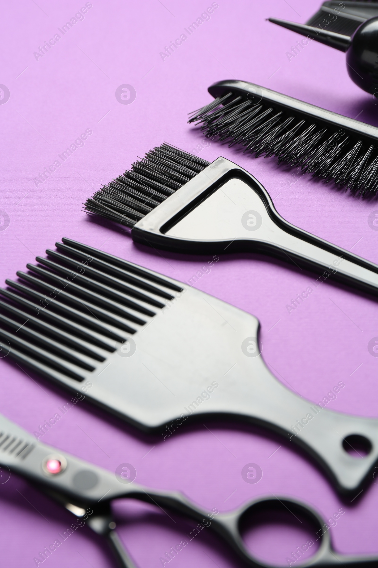 Photo of Different hairdresser's tools on violet background, closeup