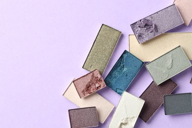 Photo of Beautiful eyeshadow refill pans on lilac background, flat lay. Space for text