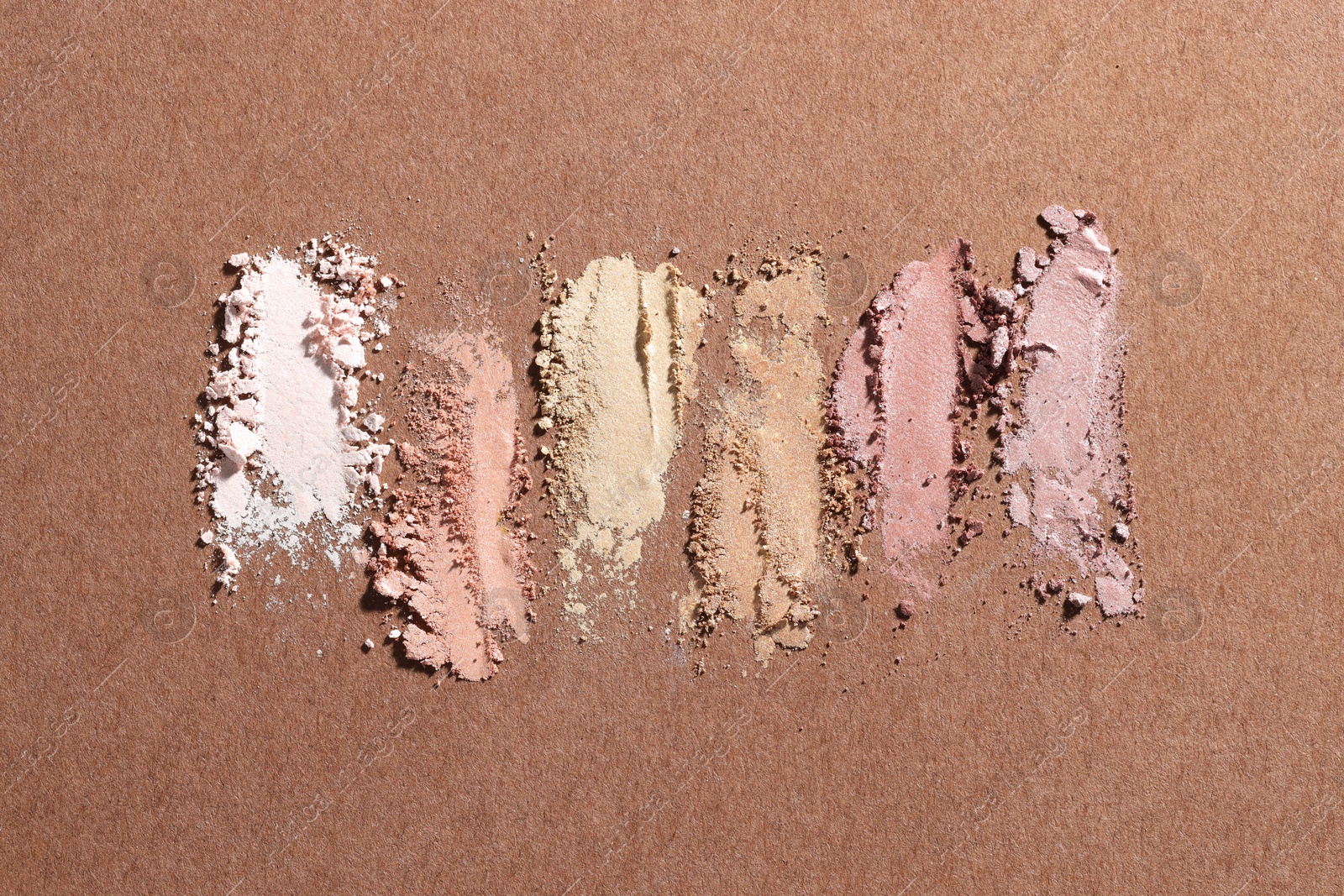 Different eyeshadows smudges on brown background, flat lay Photo of Different eyeshadows smudges on brown background, flat lay