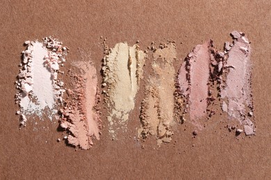 Photo of Different eyeshadows smudges on brown background, flat lay