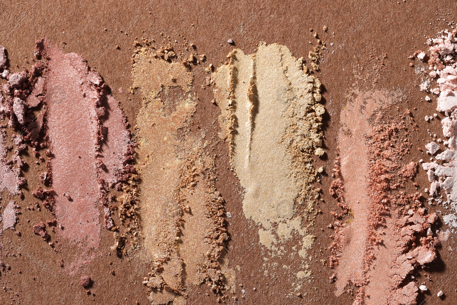 Different eyeshadows smudges on brown background, flat lay Photo of Different eyeshadows smudges on brown background, flat lay