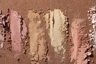 Photo of Different eyeshadows smudges on brown background, flat lay