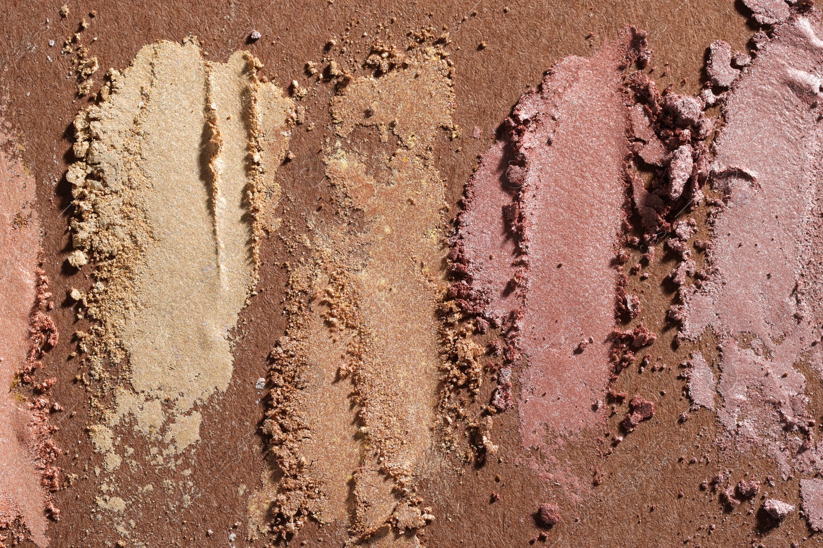 Photo of Different eyeshadows smudges on brown background, flat lay