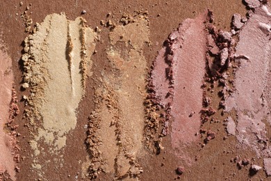 Photo of Different eyeshadows smudges on brown background, flat lay
