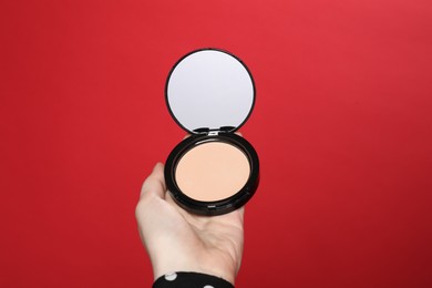 Photo of Woman holding open face powder with mirror on red background, closeup