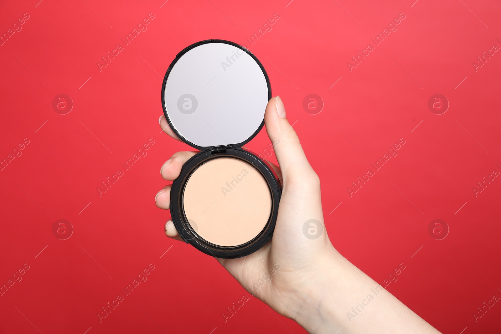 Woman holding open face powder with mirror on red background, closeup Photo of Woman holding open face powder with mirror on red background, closeup