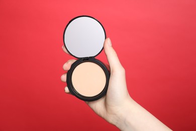 Photo of Woman holding open face powder with mirror on red background, closeup