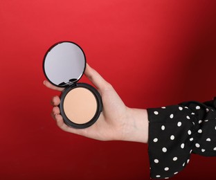 Photo of Woman holding open face powder with mirror on red background, closeup