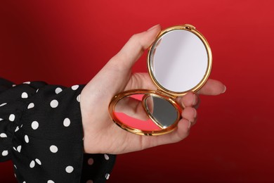 Photo of Woman holding open pocket mirror on red background, closeup