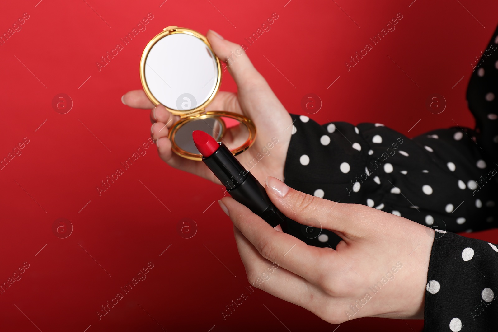 Woman holding open pocket mirror and lipstick on red background, closeup Photo of Woman holding open pocket mirror and lipstick on red background, closeup