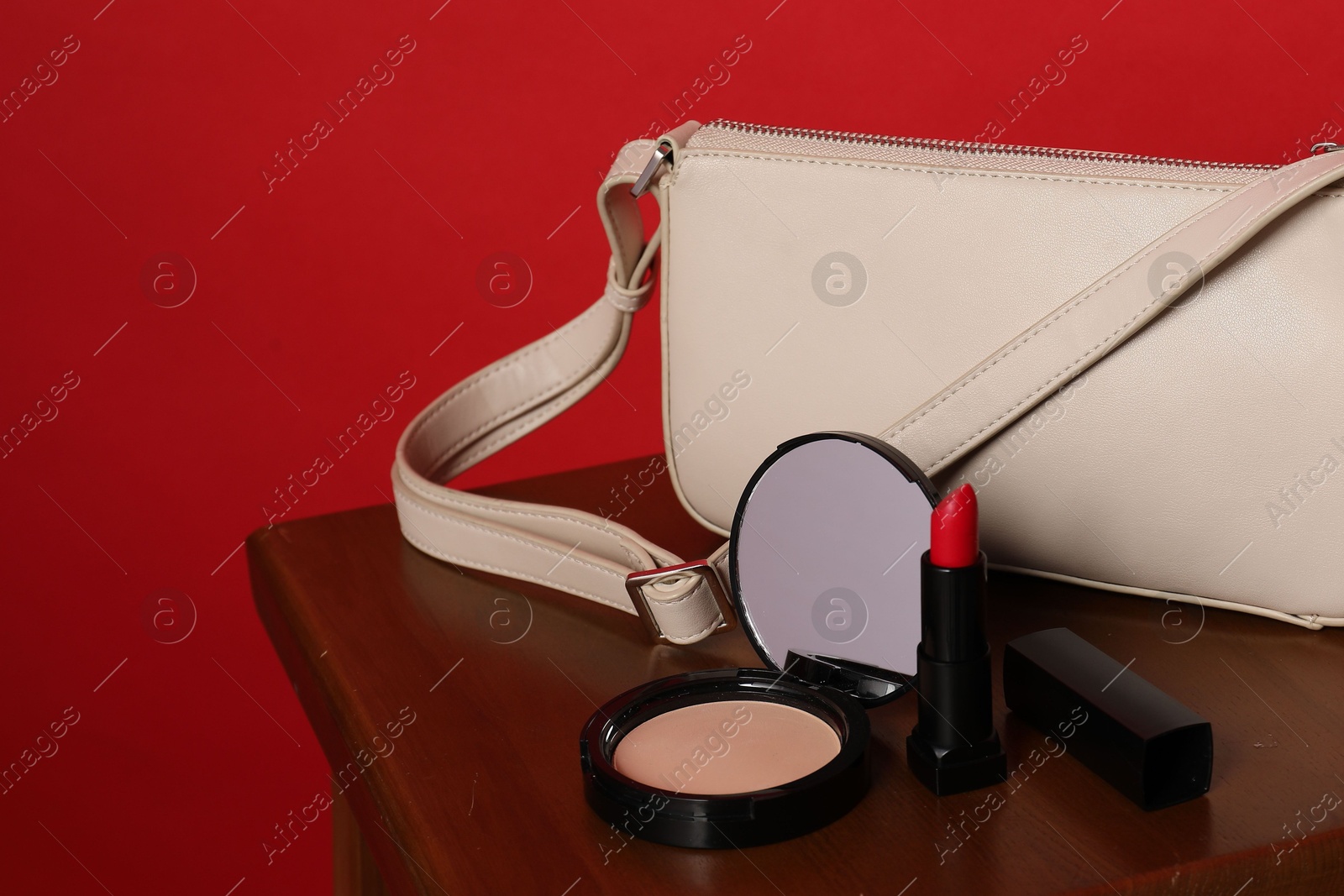 Open face powder with mirror, lipstick and bag on wooden stool against red background, closeup Photo of Open face powder with mirror, lipstick and bag on wooden stool against red background, closeup