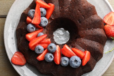Photo of Tasty chocolate bundt cake with berries on wooden table, top view