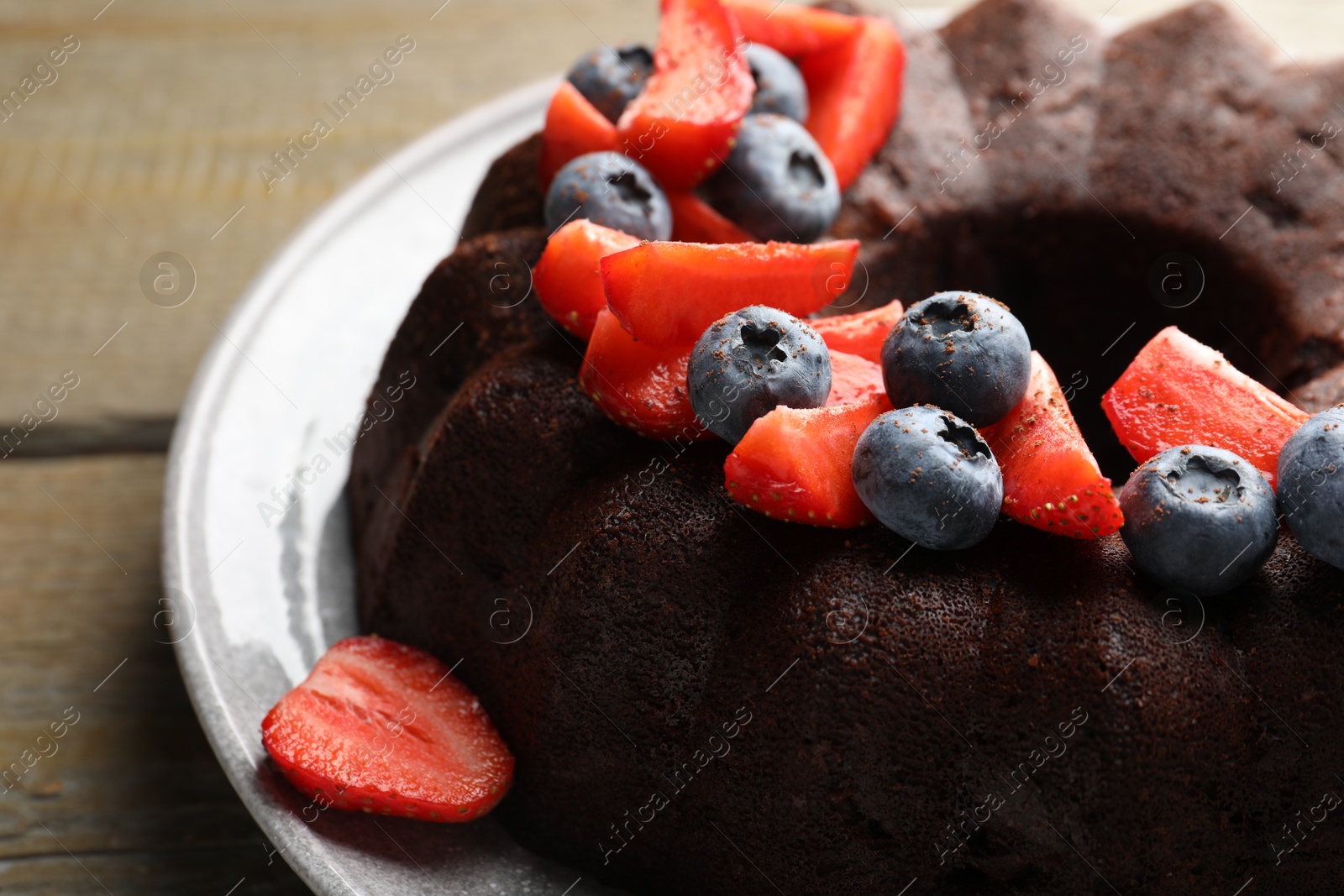 Tasty chocolate bundt cake with berries on wooden table, closeup Photo of Tasty chocolate bundt cake with berries on wooden table, closeup