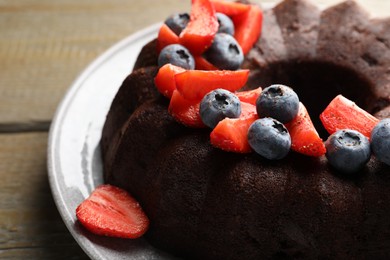 Photo of Tasty chocolate bundt cake with berries on wooden table, closeup