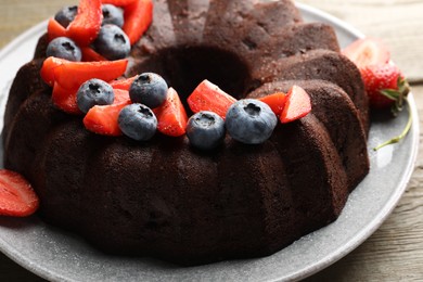 Photo of Tasty chocolate bundt cake with berries on wooden table, closeup