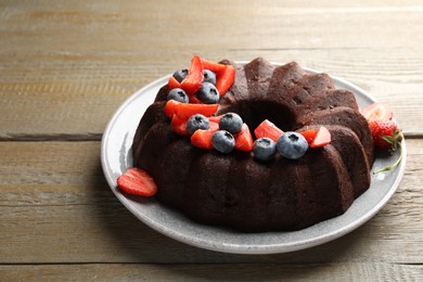 Photo of Tasty chocolate bundt cake with berries on wooden table