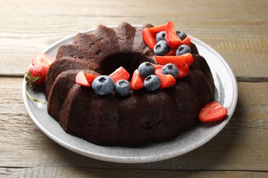 Photo of Tasty chocolate bundt cake with berries on wooden table, closeup