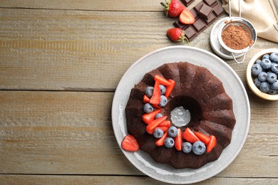 Photo of Tasty chocolate bundt cake with berries on wooden table, flat lay. Space for text