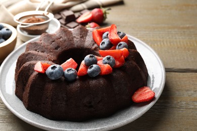 Photo of Tasty chocolate bundt cake with berries on wooden table, closeup