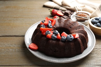 Photo of Tasty chocolate bundt cake with berries on wooden table. Space for text