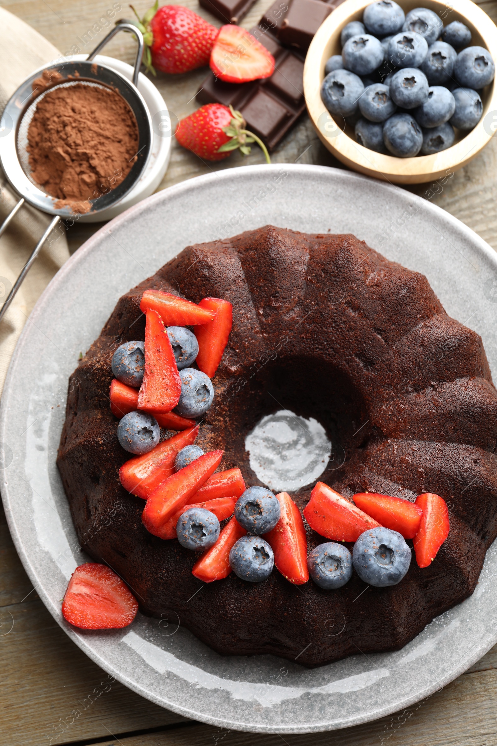 Tasty chocolate bundt cake with berries on wooden table, flat lay Photo of Tasty chocolate bundt cake with berries on wooden table, flat lay