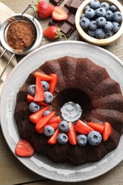 Photo of Tasty chocolate bundt cake with berries on wooden table, flat lay