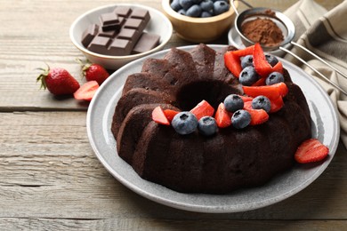 Photo of Tasty chocolate bundt cake with berries on wooden table, closeup