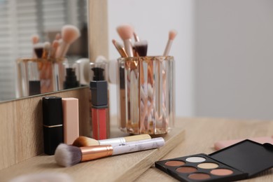 Photo of Different makeup products and brushes on vanity indoors, closeup