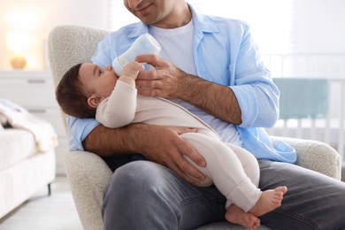 Photo of Father feeding his little baby with bottle on armchair at home, closeup