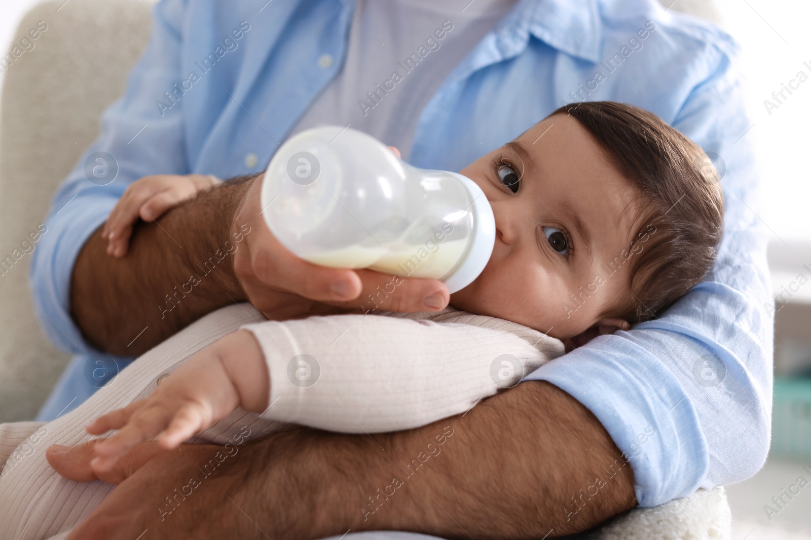 Father feeding his little baby with bottle on armchair at home, closeup Photo of Father feeding his little baby with bottle on armchair at home, closeup