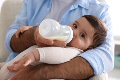 Photo of Father feeding his little baby with bottle on armchair at home, closeup