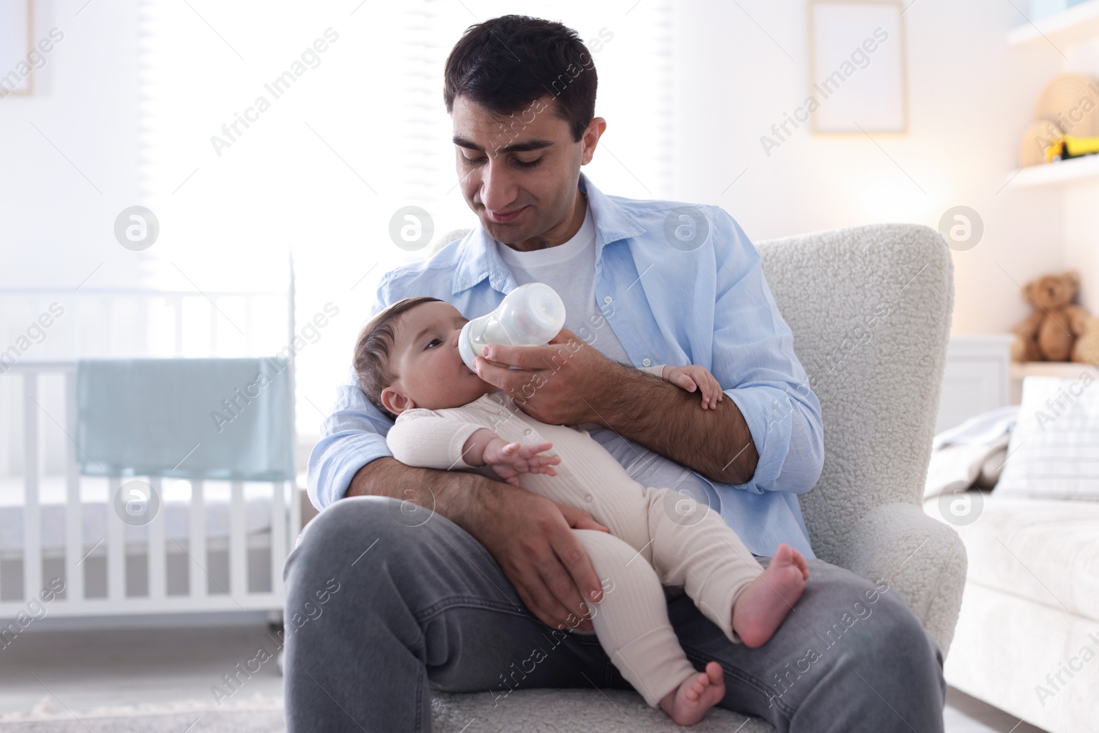 Father feeding his little baby with bottle on armchair at home Photo of Father feeding his little baby with bottle on armchair at home