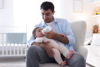 Photo of Father feeding his little baby with bottle on armchair at home