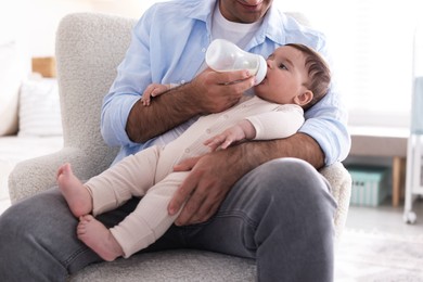 Photo of Father feeding his little baby with bottle on armchair at home, closeup