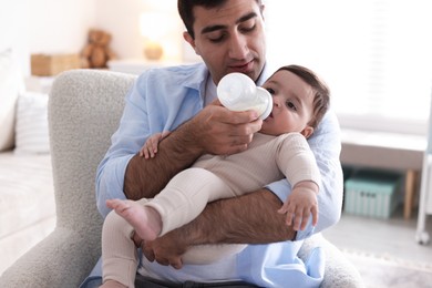 Photo of Father feeding his little baby with bottle on armchair at home