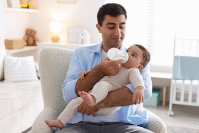 Photo of Father feeding his little baby with bottle on armchair at home